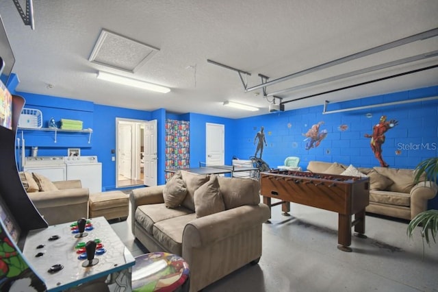 recreation room featuring concrete floors, attic access, a garage, independent washer and dryer, and concrete block wall