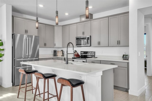 kitchen with a kitchen bar, a kitchen island with sink, appliances with stainless steel finishes, and gray cabinetry