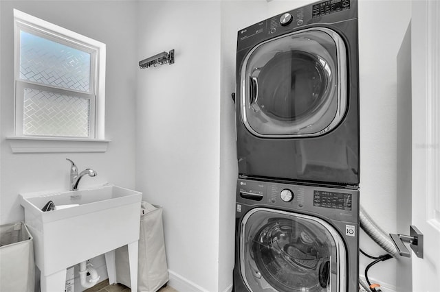 laundry area featuring laundry area, stacked washer / dryer, baseboards, and a sink