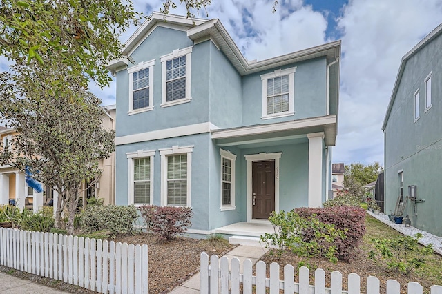 traditional home featuring a fenced front yard, a porch, and stucco siding