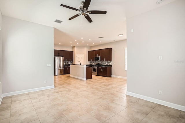 kitchen featuring open floor plan, an island with sink, decorative backsplash, stainless steel appliances, and a ceiling fan