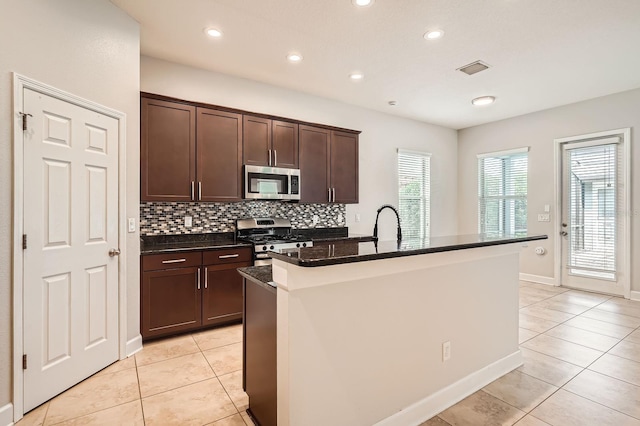 kitchen with a center island with sink, stainless steel appliances, light tile patterned floors, decorative backsplash, and dark brown cabinets