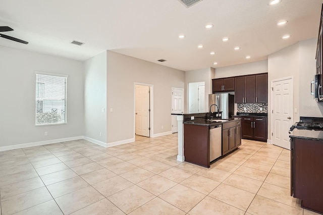 kitchen featuring visible vents, a center island with sink, a ceiling fan, stainless steel appliances, and decorative backsplash