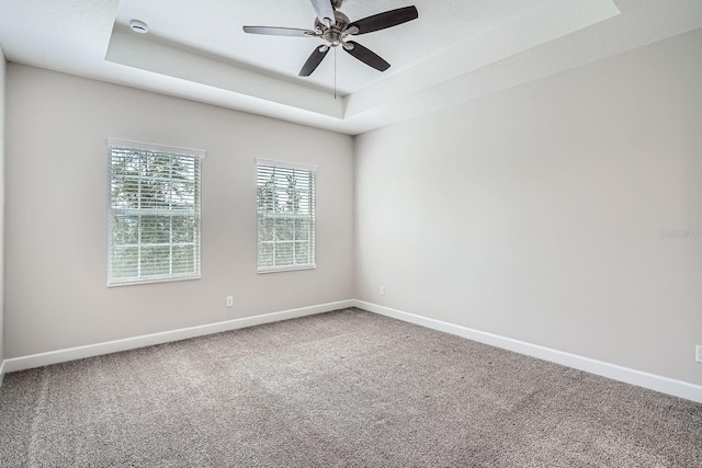 carpeted spare room with ceiling fan, a raised ceiling, and baseboards