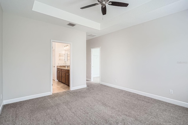 unfurnished bedroom featuring visible vents, baseboards, a tray ceiling, light carpet, and ensuite bath