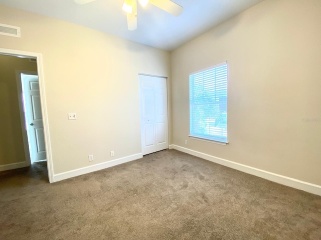 unfurnished bedroom with visible vents, dark carpet, a closet, baseboards, and ceiling fan