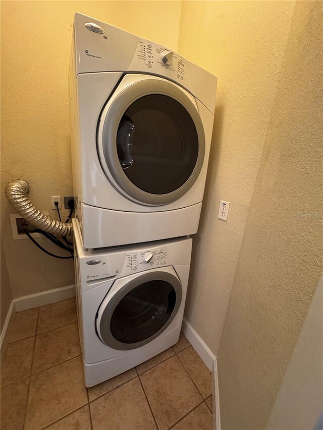 laundry room with light tile patterned flooring, stacked washer / dryer, laundry area, and baseboards