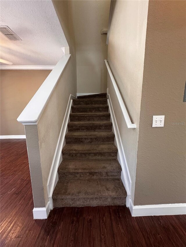 stairway with a textured ceiling, wood finished floors, visible vents, and baseboards