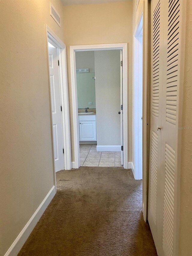 corridor featuring light carpet, visible vents, baseboards, and a sink