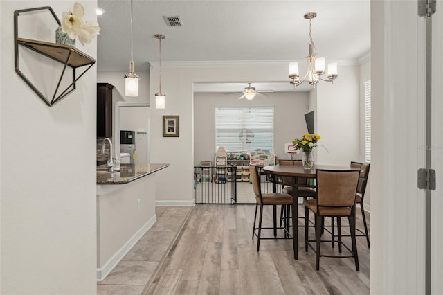 dining space with a ceiling fan, baseboards, visible vents, ornamental molding, and light wood-type flooring