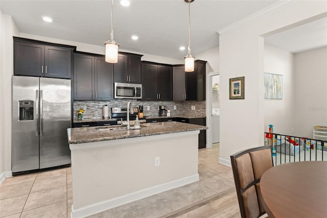 kitchen featuring backsplash, a center island with sink, dark stone counters, stainless steel appliances, and a sink