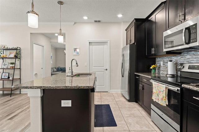 kitchen featuring light stone counters, a center island with sink, a sink, decorative backsplash, and stainless steel appliances