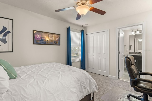 carpeted bedroom featuring a closet, ensuite bathroom, and a ceiling fan