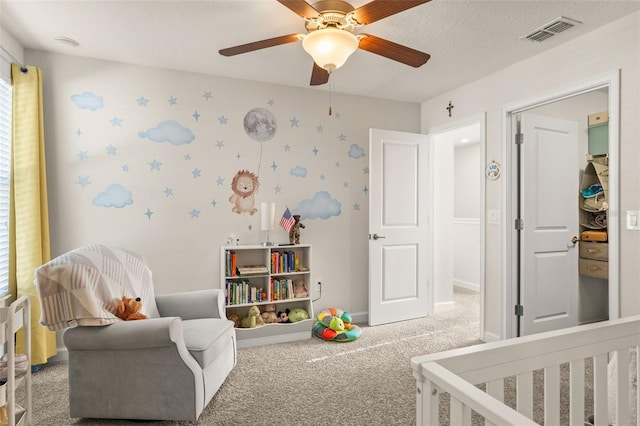 carpeted bedroom with visible vents, a nursery area, a ceiling fan, and baseboards