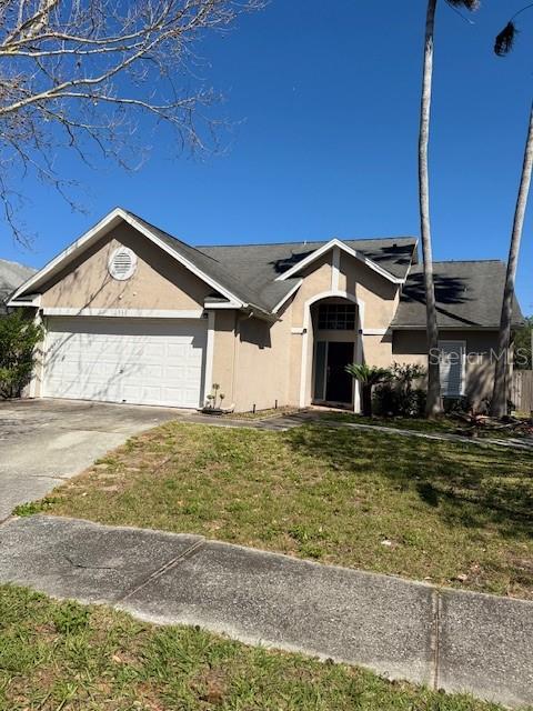 ranch-style home with stucco siding, a front lawn, an attached garage, and driveway