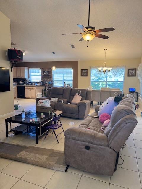 living area with light tile patterned floors, ceiling fan with notable chandelier, visible vents, and a textured ceiling