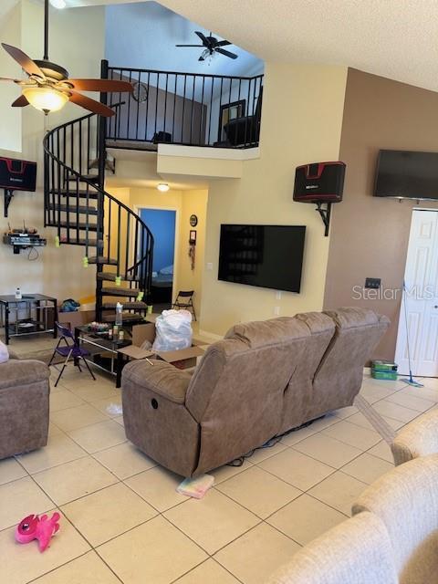 living area featuring ceiling fan, stairway, a towering ceiling, tile patterned floors, and a textured ceiling