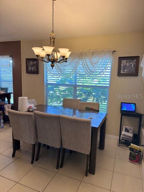 dining room featuring a textured ceiling, light tile patterned floors, baseboards, and a chandelier