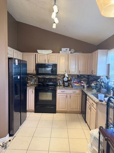 kitchen featuring light tile patterned floors, black appliances, tasteful backsplash, and vaulted ceiling