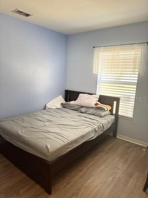 bedroom featuring visible vents, multiple windows, baseboards, and wood finished floors