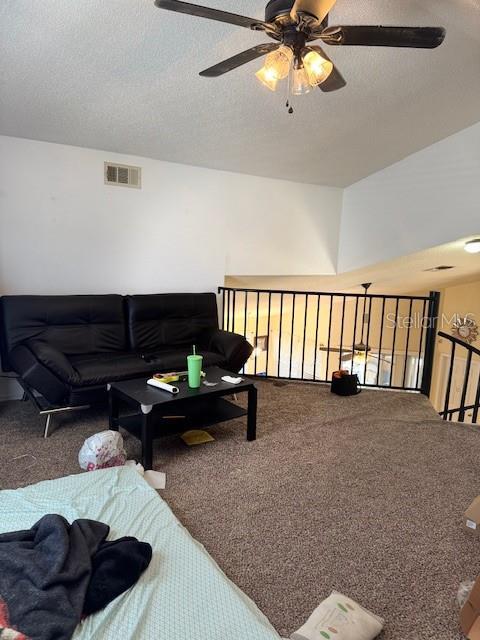 carpeted living room with a textured ceiling, visible vents, and ceiling fan