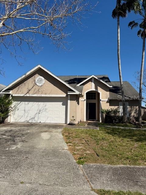 ranch-style home with a garage, concrete driveway, a front yard, and stucco siding