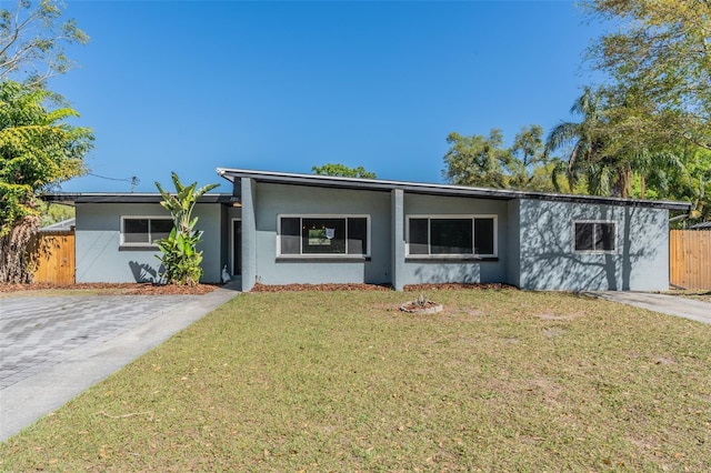 view of front of property featuring stucco siding, driveway, a front lawn, and fence