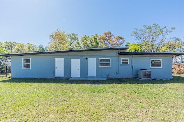 rear view of property with stucco siding, cooling unit, a yard, and fence