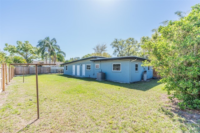 back of property featuring a fenced backyard, a lawn, central AC, and stucco siding