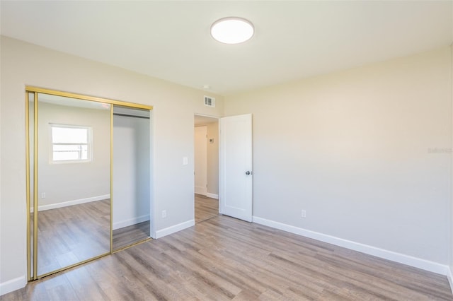 unfurnished bedroom with wood finished floors, visible vents, a closet, and baseboards