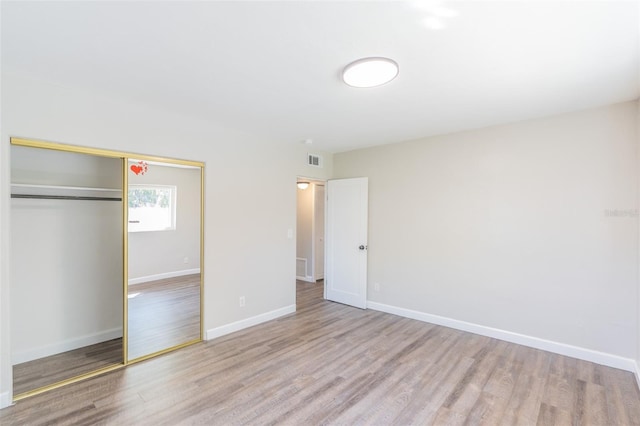 unfurnished bedroom featuring visible vents, baseboards, a closet, and wood finished floors