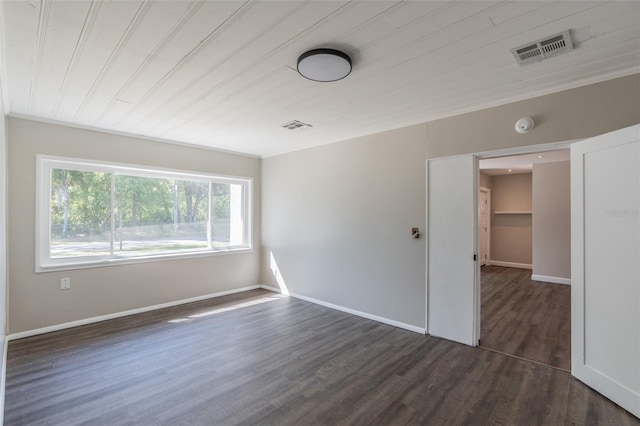 empty room featuring visible vents, dark wood-type flooring, and baseboards