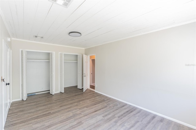 unfurnished bedroom featuring visible vents, two closets, wood finished floors, and ornamental molding