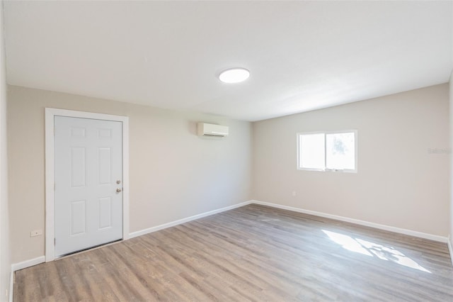 empty room featuring wood finished floors, baseboards, and a wall mounted AC