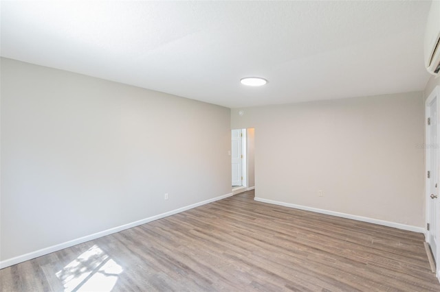 empty room featuring baseboards, light wood-type flooring, and a wall mounted AC