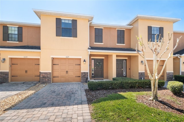 multi unit property with stucco siding, stone siding, a garage, and decorative driveway