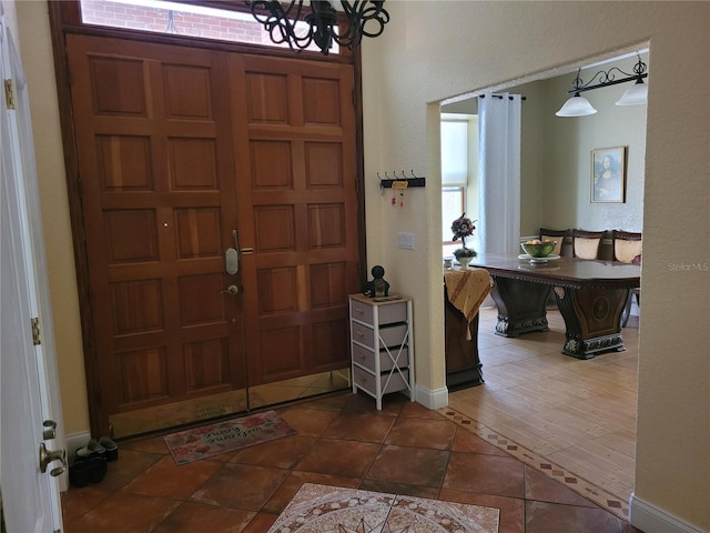 tiled entrance foyer featuring baseboards and a notable chandelier