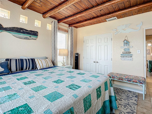 bedroom featuring tile patterned floors, beamed ceiling, a closet, wood ceiling, and a textured wall