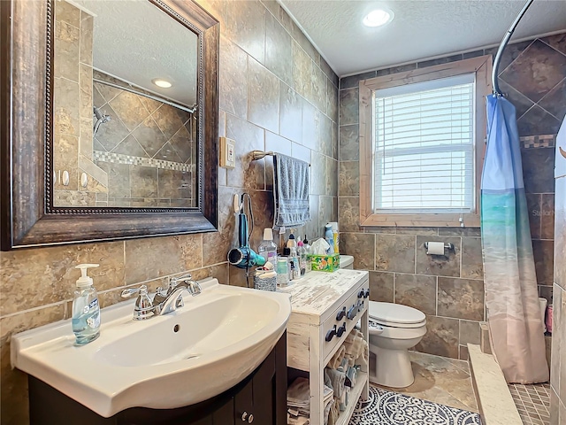 bathroom with toilet, a textured ceiling, a tile shower, tile walls, and vanity