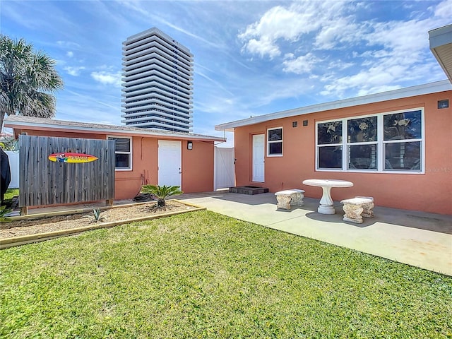 rear view of property featuring an outbuilding, a lawn, a patio, and stucco siding