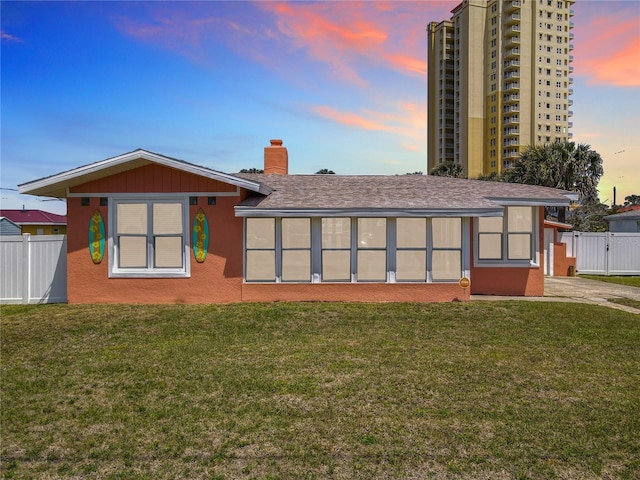 rear view of property featuring a chimney, a lawn, fence, and stucco siding