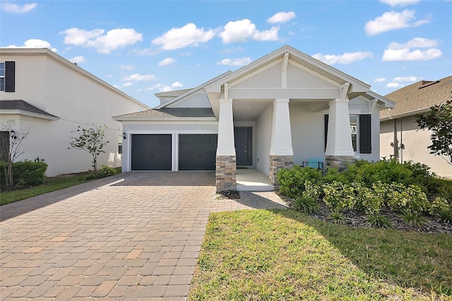 view of front of property with decorative driveway, an attached garage, stone siding, and stucco siding