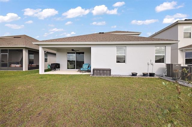 rear view of house with ceiling fan, stucco siding, cooling unit, a lawn, and a patio