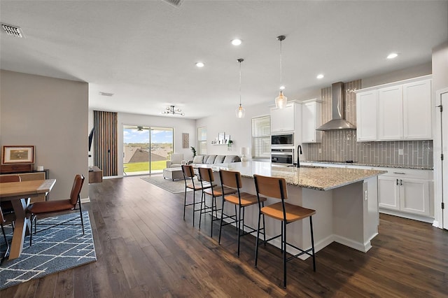 kitchen with tasteful backsplash, visible vents, built in microwave, open floor plan, and wall chimney exhaust hood