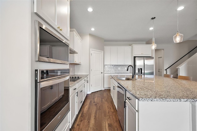 kitchen with a sink, a center island with sink, decorative backsplash, stainless steel appliances, and dark wood-style flooring