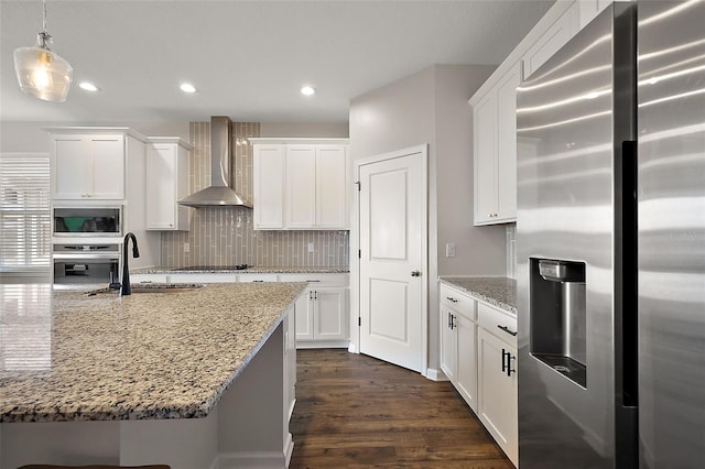 kitchen with backsplash, dark wood-type flooring, appliances with stainless steel finishes, wall chimney exhaust hood, and a sink