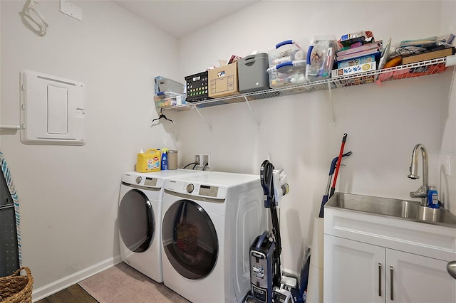 washroom featuring baseboards, electric panel, cabinet space, a sink, and washer and clothes dryer