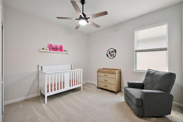 bedroom featuring a crib, carpet flooring, baseboards, and ceiling fan