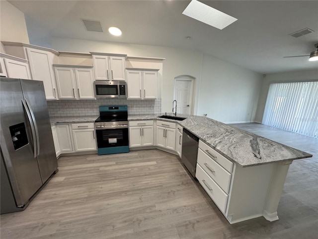 kitchen with backsplash, light stone counters, appliances with stainless steel finishes, a peninsula, and a sink