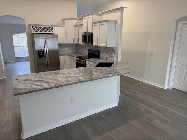 kitchen with a sink, arched walkways, appliances with stainless steel finishes, decorative backsplash, and light stone countertops